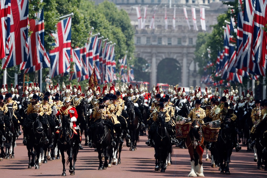 Formally dressed soldiers sit atop of horses in a parade lined with British flags