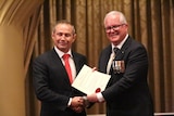Two men shake hands while wearing suits an official document.