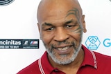 Mike Tyson smiles at a camera wearing a red polo shirt