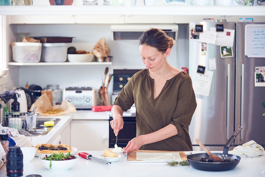 A woman assembles a puff pastry tart with mushrooms and cheese in her home kitchen.