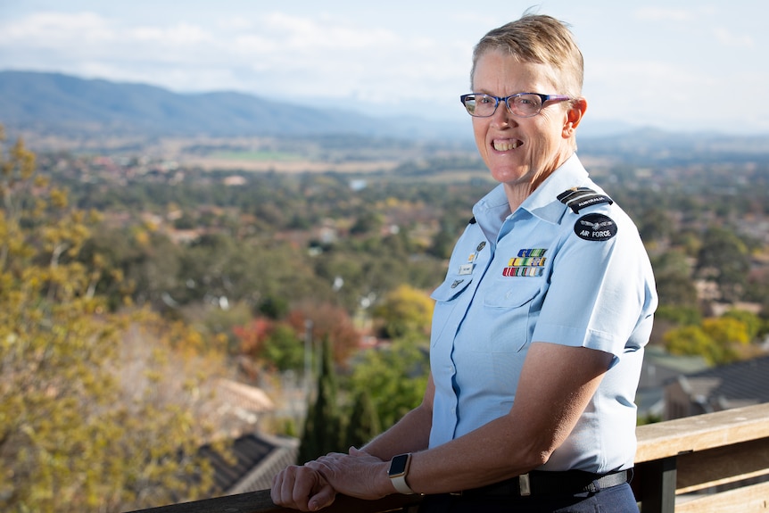 A woman in military uniform outdoors, smiling.