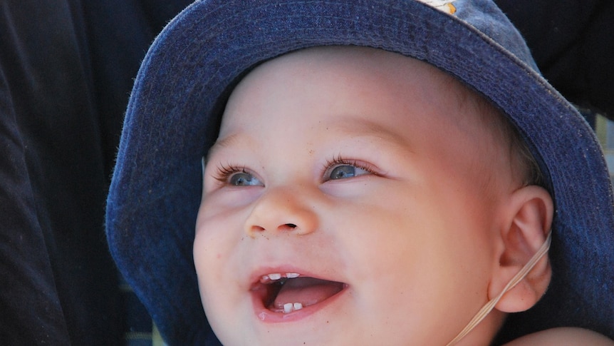A baby is smiling showing a few teeth