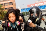 Two riot police with helmets, masks and breathing equipment pull a female protester down the street.