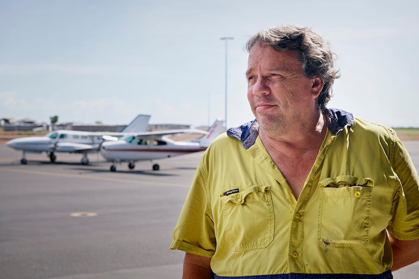 A man stands in front of planes and looks into the distance. 