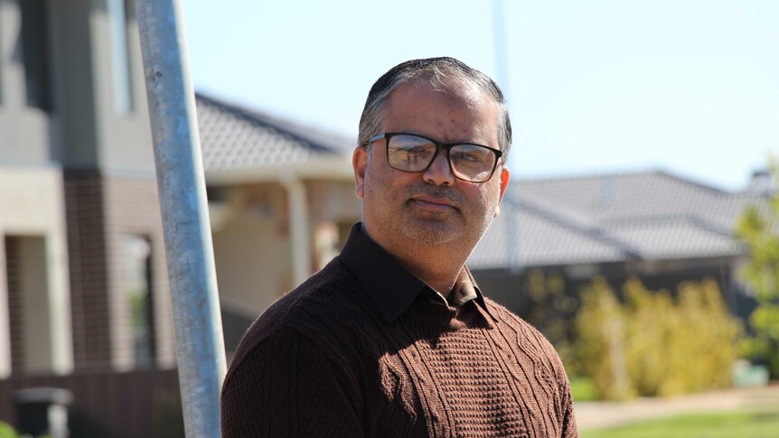 Imran Arshad, in a brown jumper and glasses, stands outside his house with a slight smile.