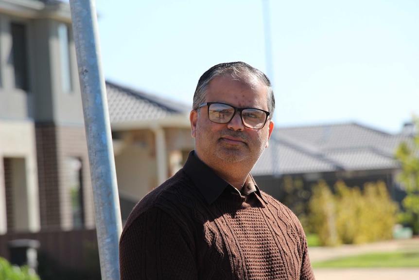 Imran Arshad, in a brown jumper and glasses, stands outside his house with a slight smile.