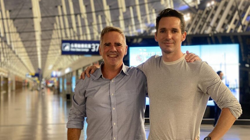 Smith and Birtles with their arms around each others shoulders, as they stand in the middle of Shanghai Airport's terminal