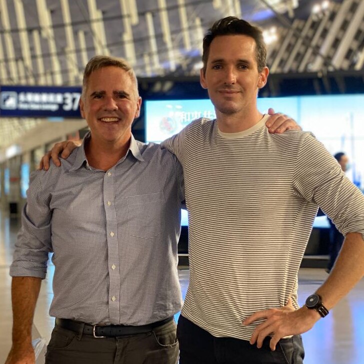 Smith and Birtles with their arms around each others shoulders, as they stand in the middle of Shanghai Airport's terminal