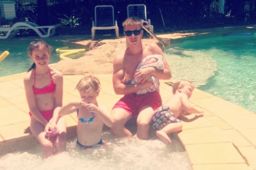 An older-looking family photo of dad with daughter and three younger children by a resort pool.