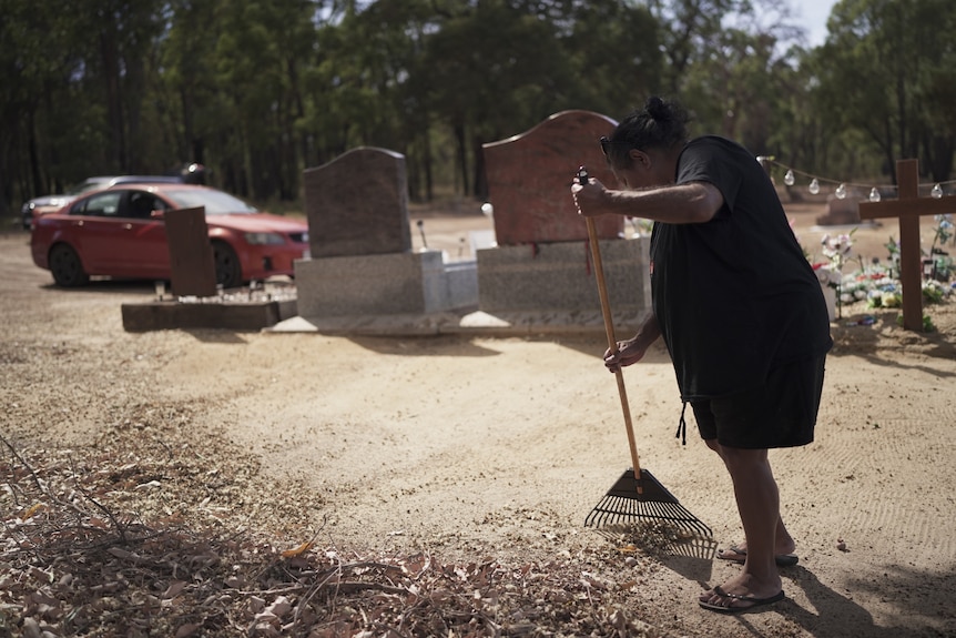 A woman in a black t-shirt rakes dirt and rocks at a cemetary