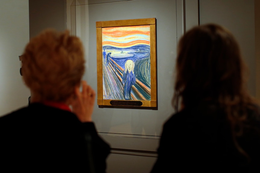 The Scream hangs on a gallery wall in a photo looking over the shoulder of two people 