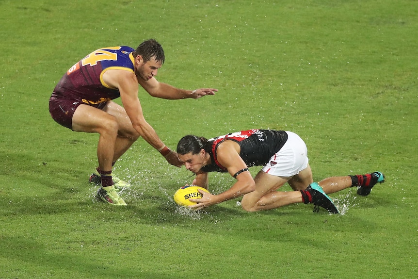 Two AFL players contest for the ball in wet conditions at the Gabba in Brisbane.