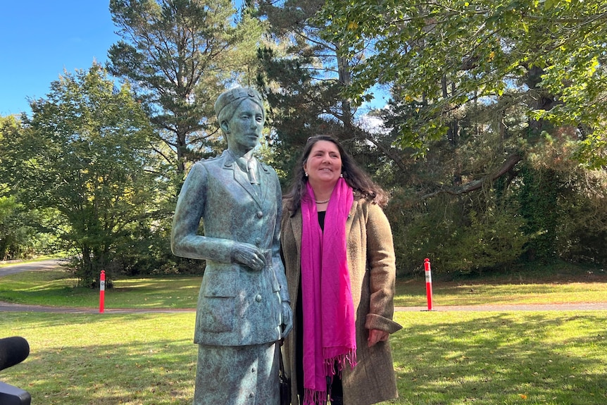 A woman wearing a bright pink scarf poses with a bronze statue in a park.