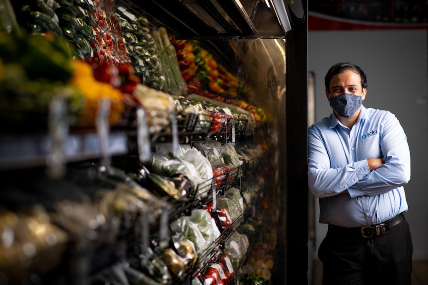 a man wearing a face mask standing near groceries