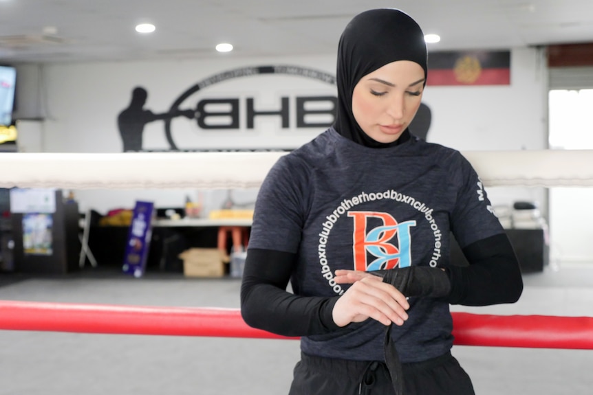 A female boxer wearing a headscarf winds black boxing straps around her hands.