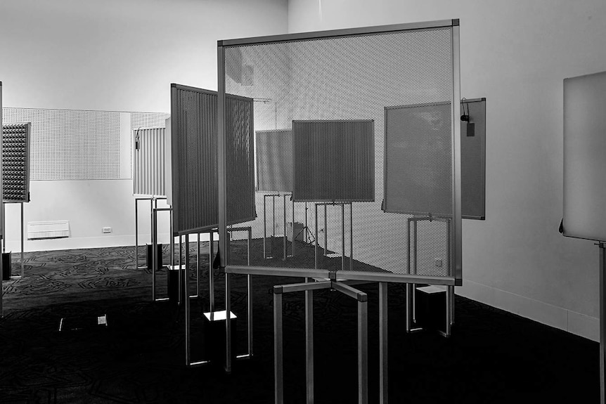 A black and white photo of a room speakers playing sounds into a with many panels mounted on stands.