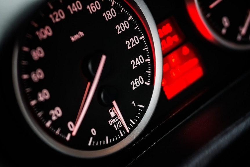 A speedometer on the dashboard of a car is lit up red, with the needle at zero. 