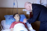 Governor-General Sir Peter Cosgrove pins a medal on Connie Johnson's chest as she lies in a bed.
