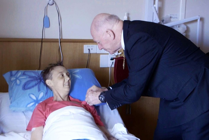Governor-General Sir Peter Cosgrove pins a medal on Connie Johnson's chest as she lies in a bed.
