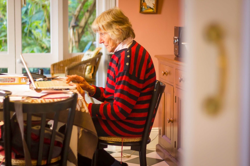 A woman in her 70s sits at home, typing letters on her laptop computer.