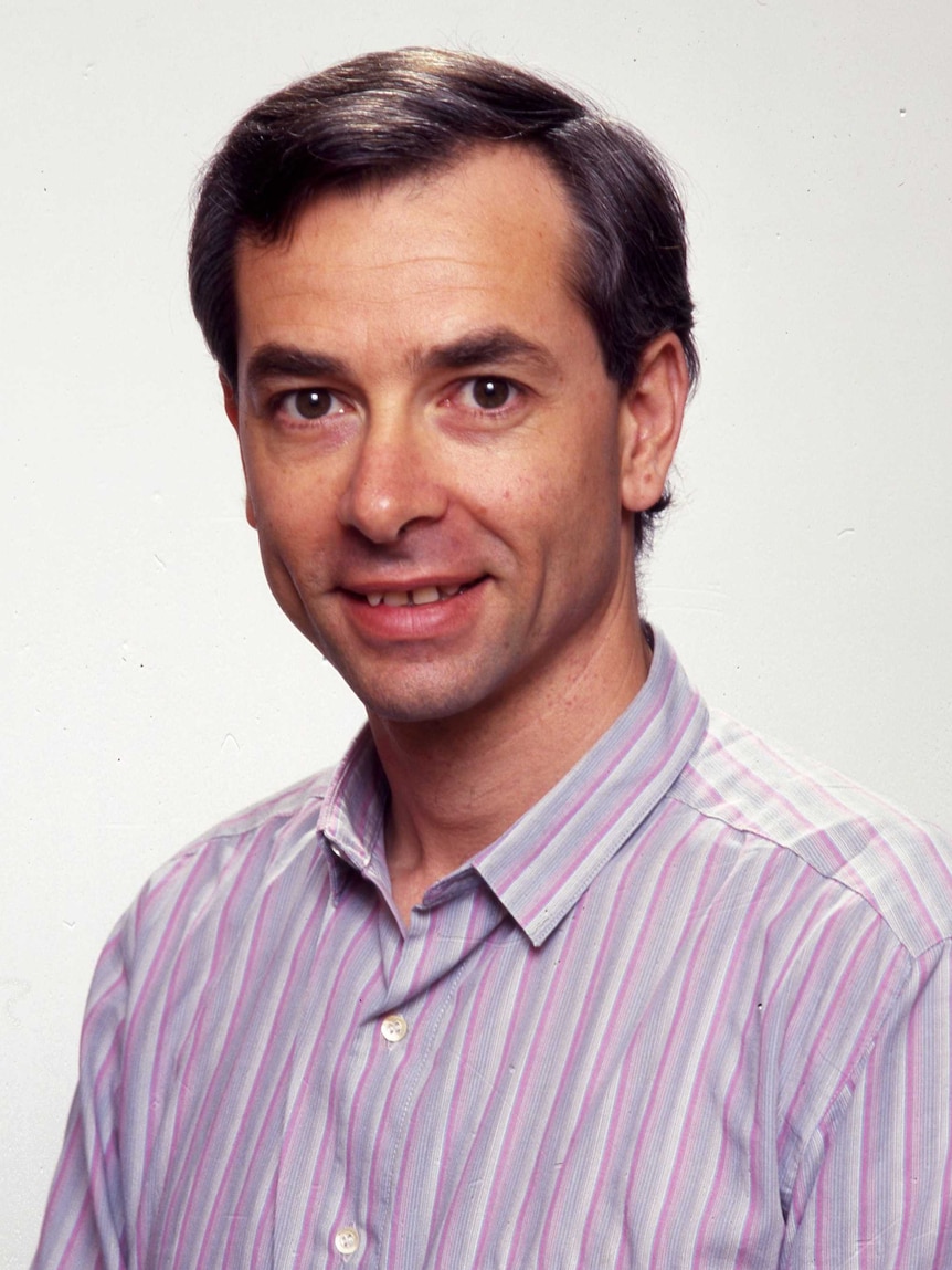 A man with neat hair and a collared shirt smiles slightly against a white background.