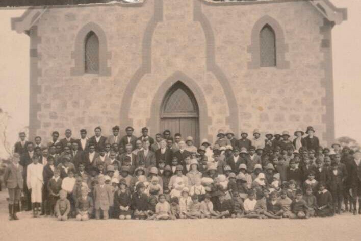Old black and whit ephoto of congregation in front of large stone building