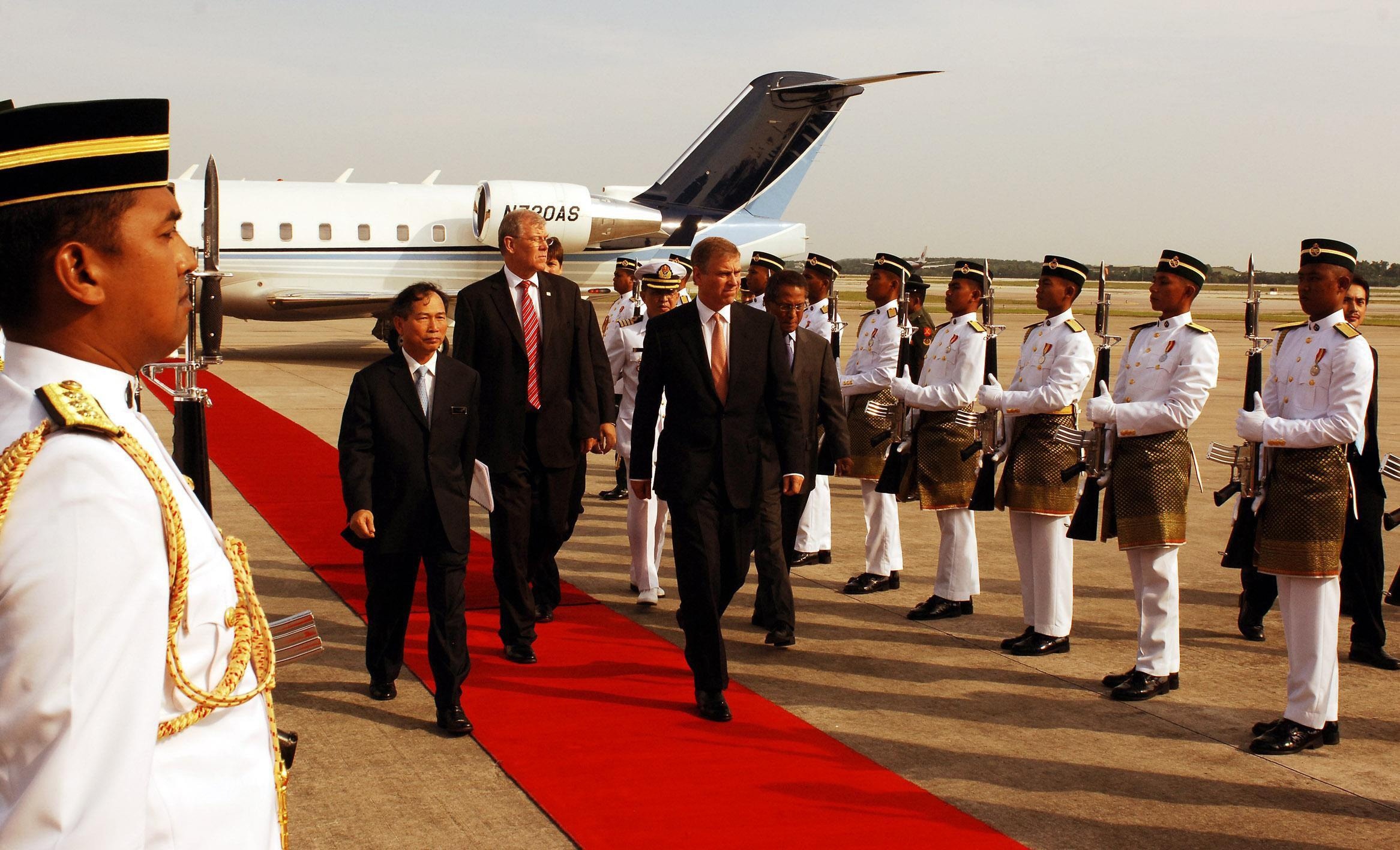 A man walks down a red carpet leading from a plane