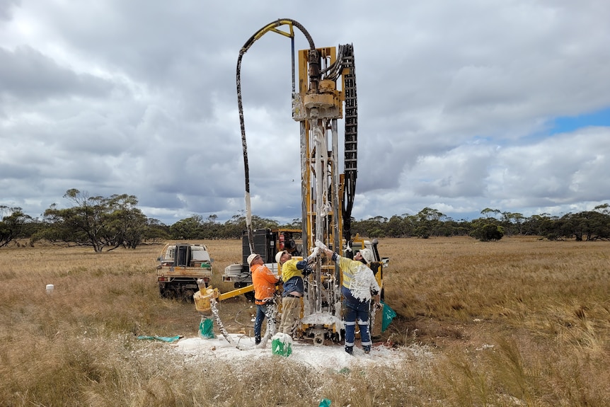 A giant drill extracts kaolin from the ground with workers covered in the material.