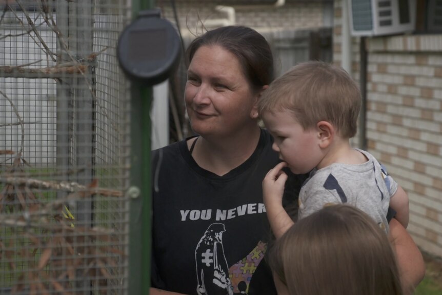 A lady holding her son and looking into a bird cage.