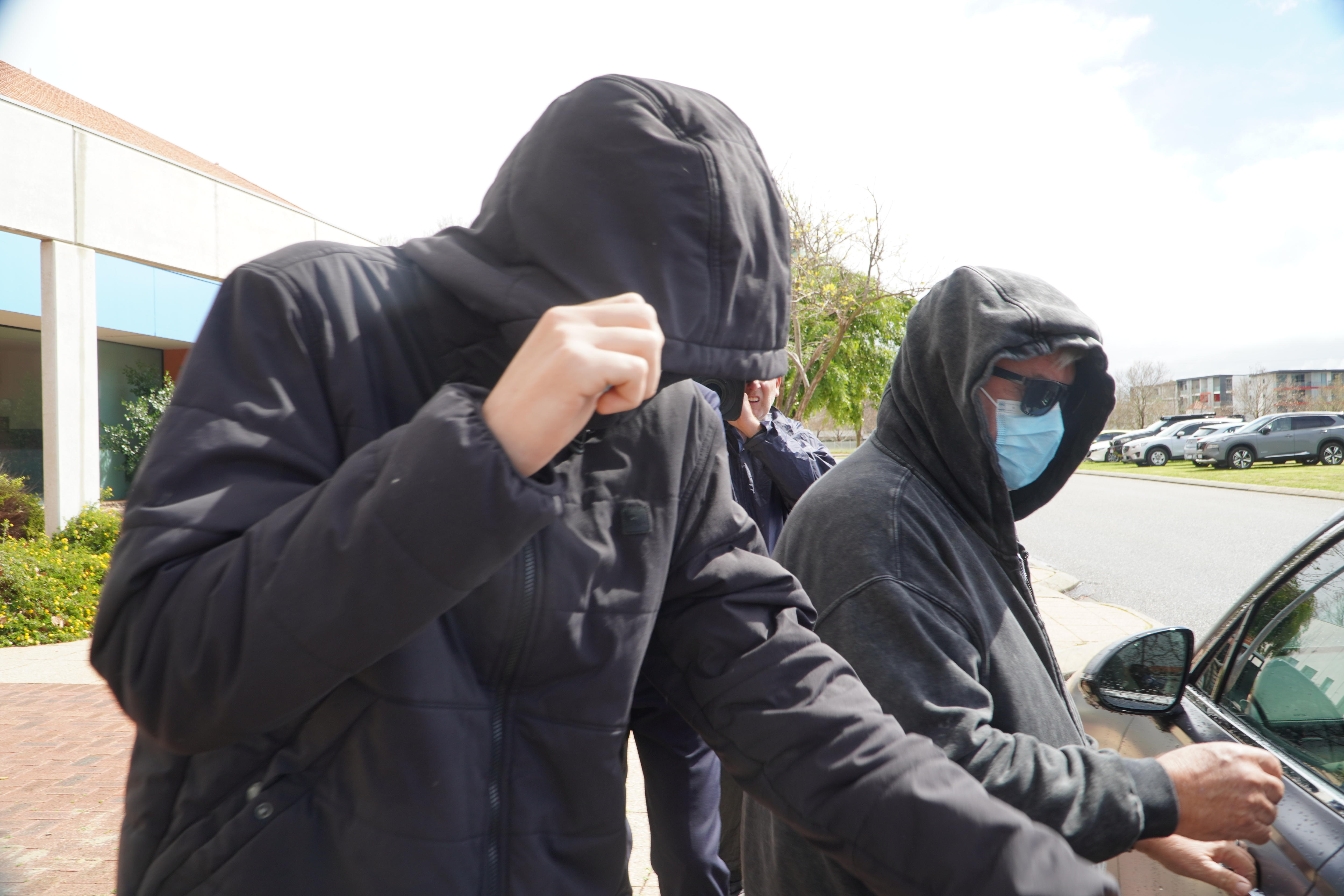 A person pulls a black hood down over his head as a reporter holds a microphone in his direction.