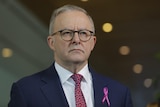 Anthony Albanese frowns while wearing a suit, tie, and pink ribbon on his lapel