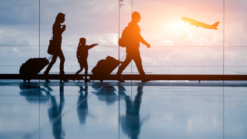 Silhouettes of a family walk past an airport window as a plane takes off outside.