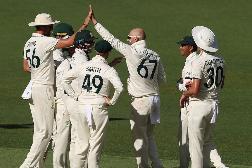 Nathan Lyon high-fives a teammate as the Australians converge in a huddle