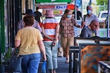 People walk up and down a suburban shopping strip, most of them wearing surgical face masks.