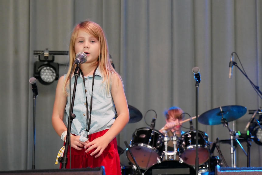 A young girl with blonde hair behind a mic on stage