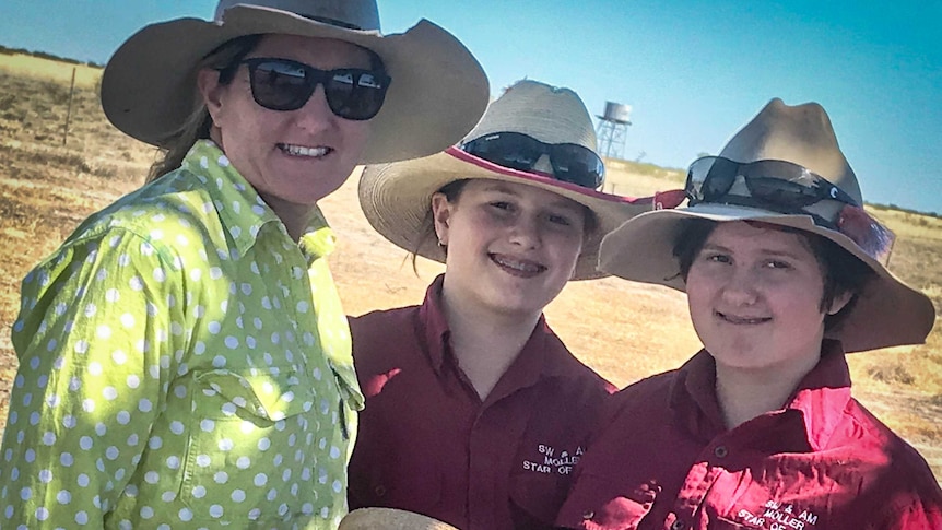 A woman in a green spotty shirt and a wide brimmed hat with her three daughters in a paddock.