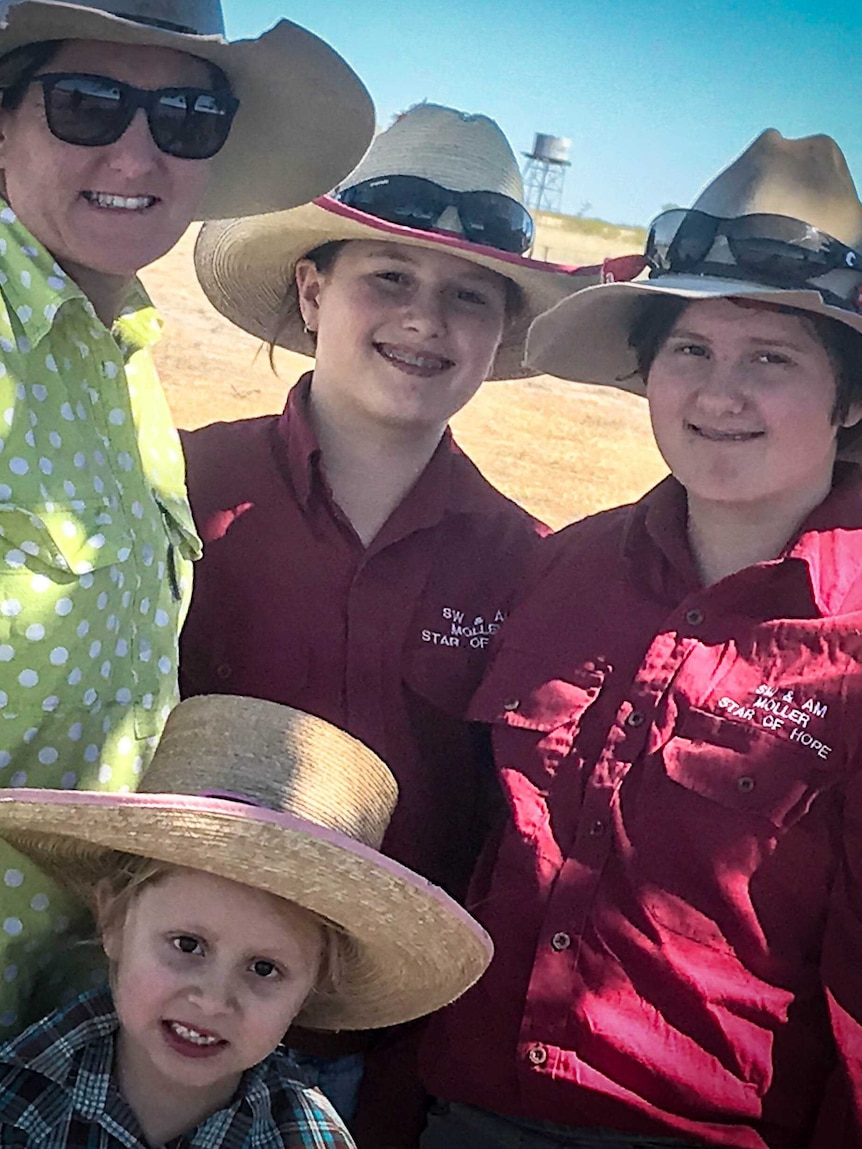 A woman in a green spotty shirt and a wide brimmed hat with her three daughters in a paddock.