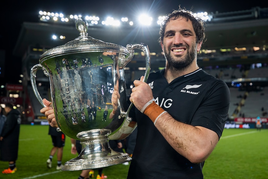 The New Zealand All Blacks captain smiles as he holds the Bledisloe Cup.