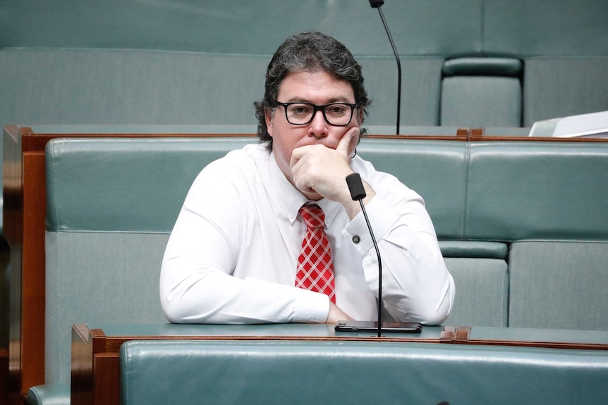 Christensen sitting forward with hand on mouth, wearing white shirt with red tie and no jacket.