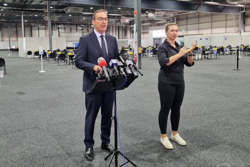 Un homme en costume parle dans une grande salle à côté d'un interprète d'Auslan