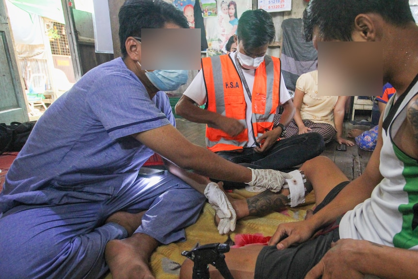 A group of people in scrubs sit on the floor surrounding a young man 