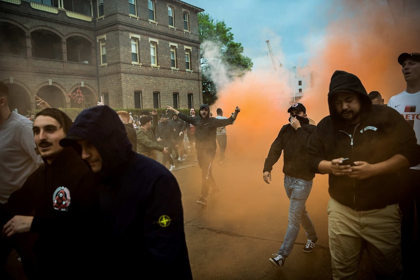 Men are seen on the street walking through flare smoke.