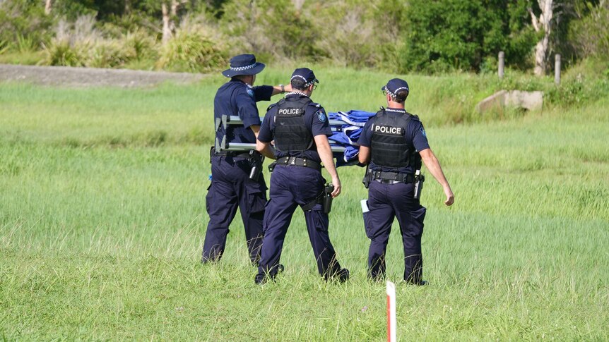 Three police officers walking on a grassy field. 