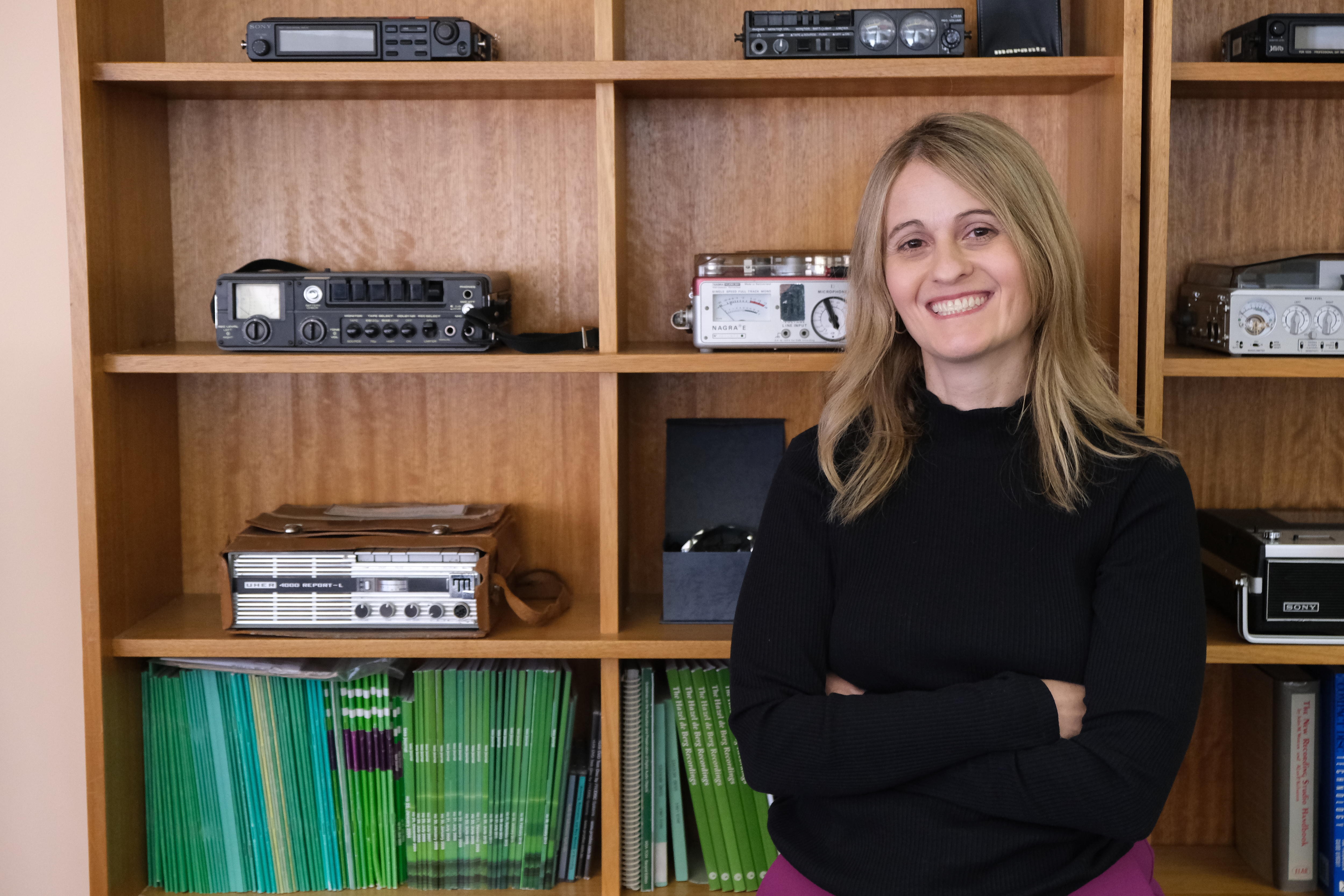 A woman stands in front of a bookcase arranged with sound record devices.