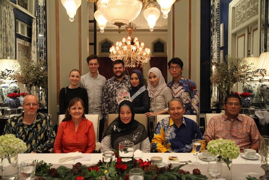 Family members from Australia and Indonesia gather for a family photo in front of a dining table.