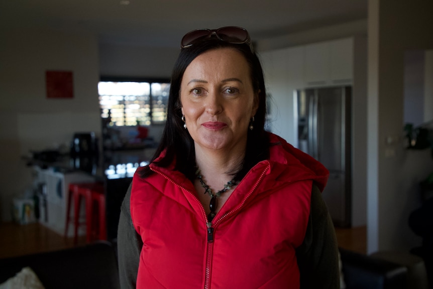Woman wearing a red puffer vest standing inside a house.