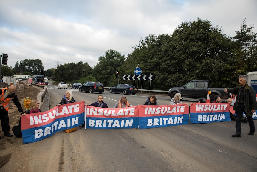 A handful of protesters with banners reading "Insulate Britain" strung across a road