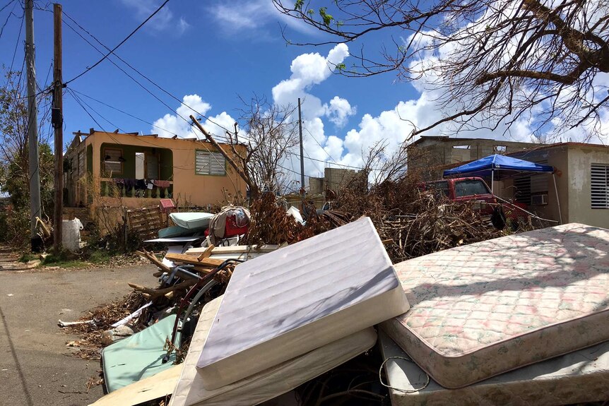 Aftermath in Puerto Rico after hurricane, mattresses, branches lie in a houses front yard