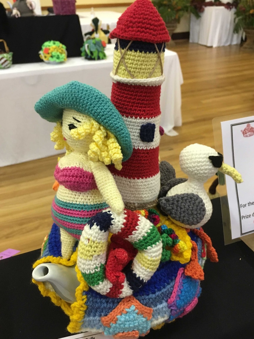A knitted teacosy featuring a girl in a hat a bikini, lighthouse and seagull