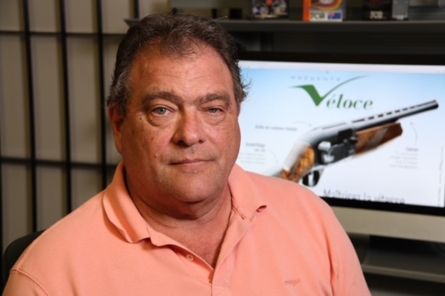 Australian Sporting Agencies CEO Rick Casagrande posing for a photo wearing a pink shirt in front of a picture of a shotgun.